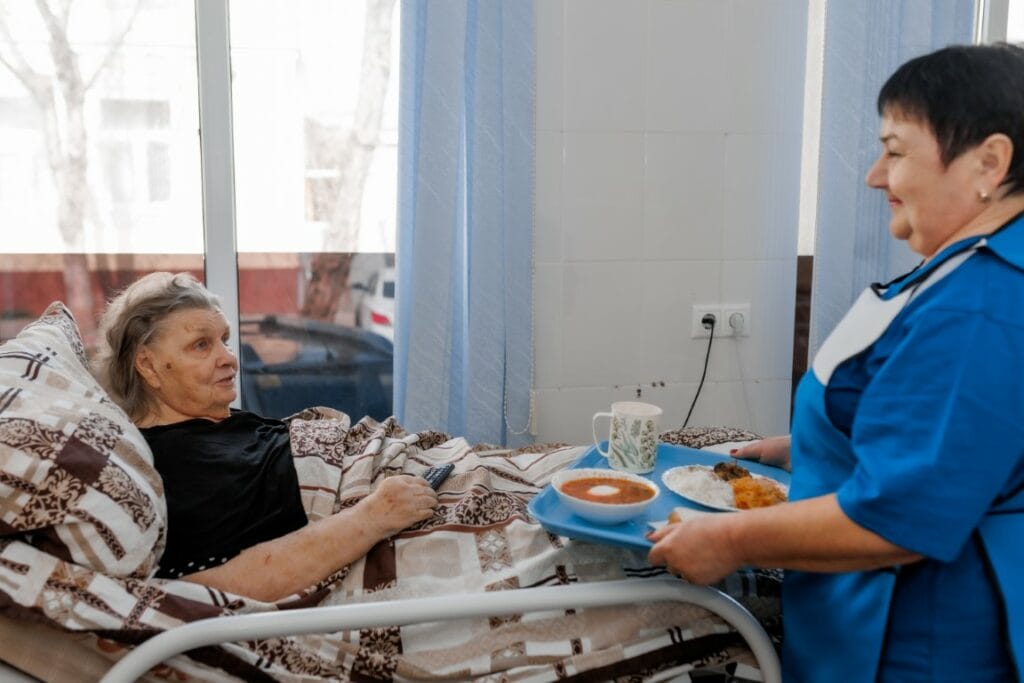 Сиделка приносит обед в постель пожилой женщине