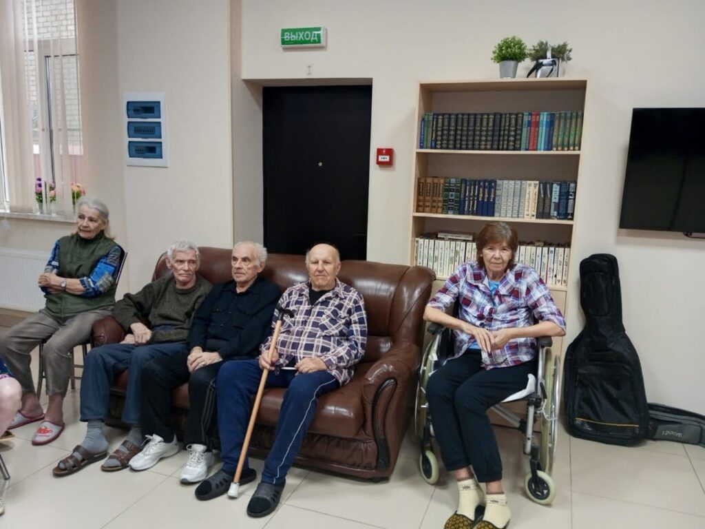 Группа пожилых людей сидит на кожаном диване